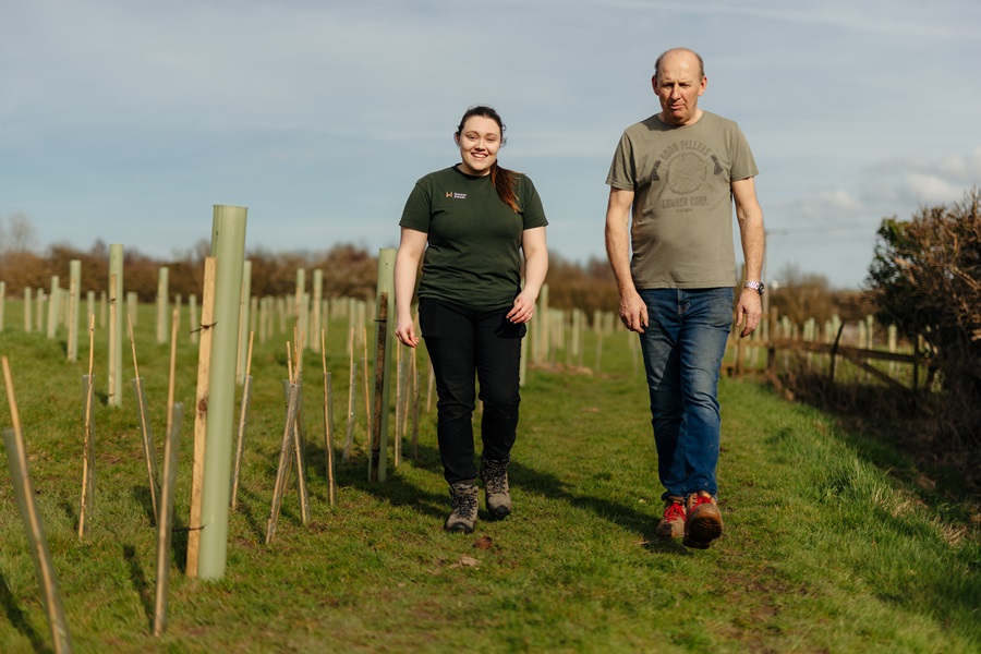 Two people having a conversation walking next to a field of newly planted trees that are protected by tree guards.